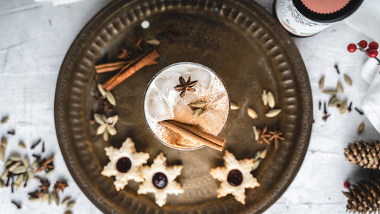 Eisgetränk mit Zimtstange, Sternanis, Keksen und Bourbon Vanille & Honig auf einem Messingtablett.