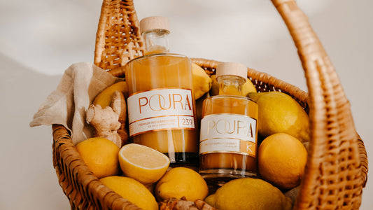 Weidenkorb mit Zitronen, Ingwer und zwei Flaschen Poura Bio Ingwer-Essenz mit orangefarbener Flüssigkeit.