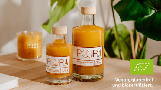 Zwei Flaschen Poura Bio Kurkuma-Essenz auf einem Tisch, Etiketten mit vegan und bio.