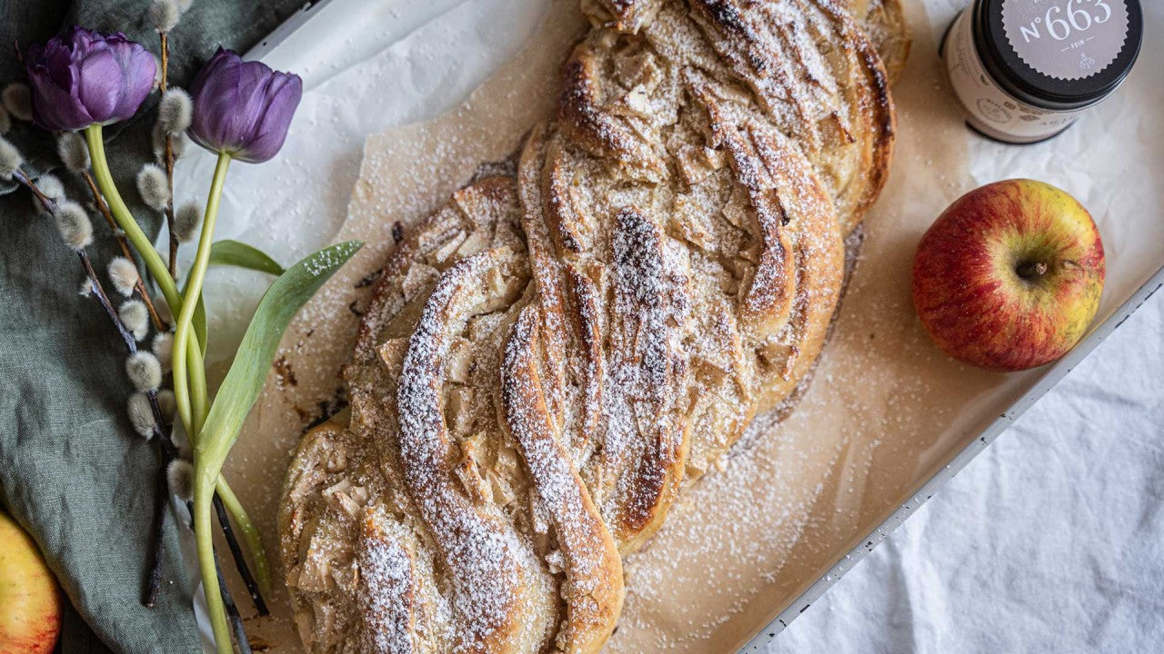Ein geflochtener Apfelkuchen mit Puderzucker, garniert mit Tulpen und Weidenkätzchen.