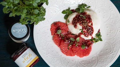 Teller mit Burrata, Grapefruit, Microgreens, roter Sauce und Gläsern Hibiskus & Honig daneben.