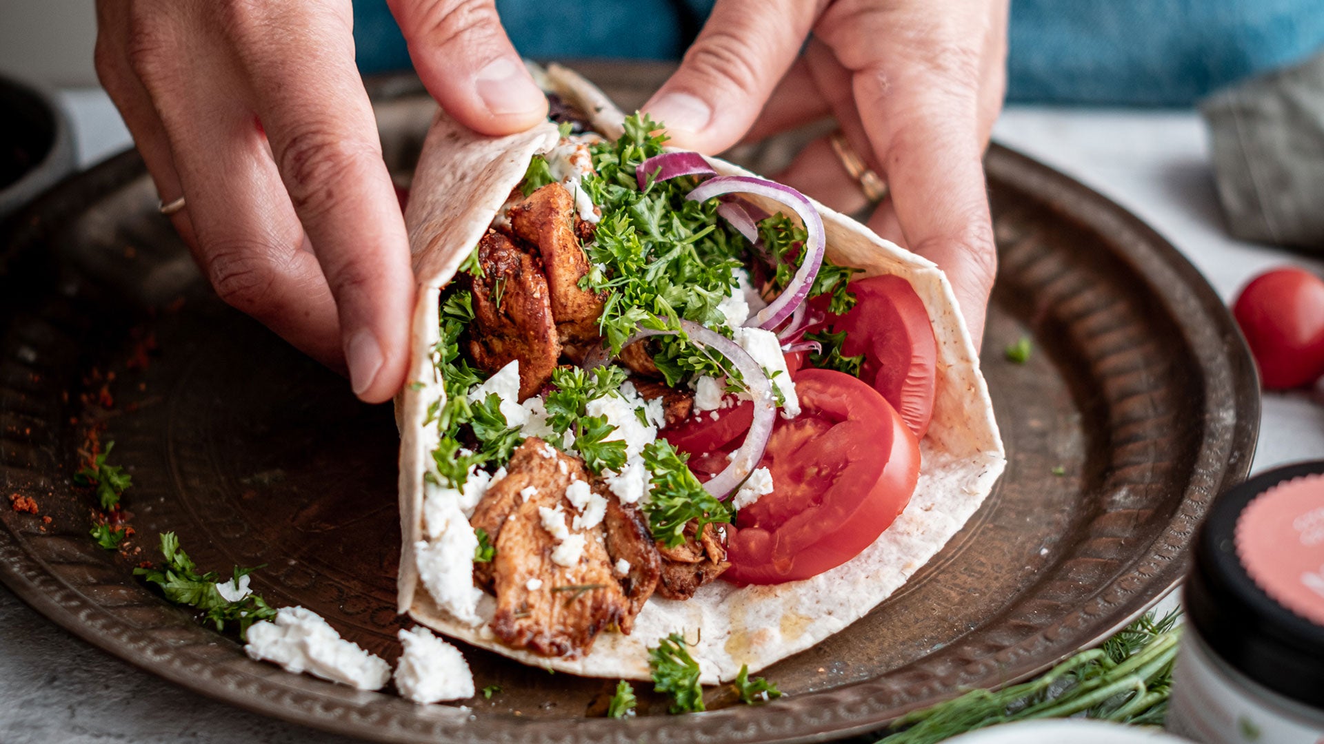 In den Händen halten sie ein Pita-Brot mit Fleisch, Feta, Tomaten, Zwiebeln und frischen Kräutern.