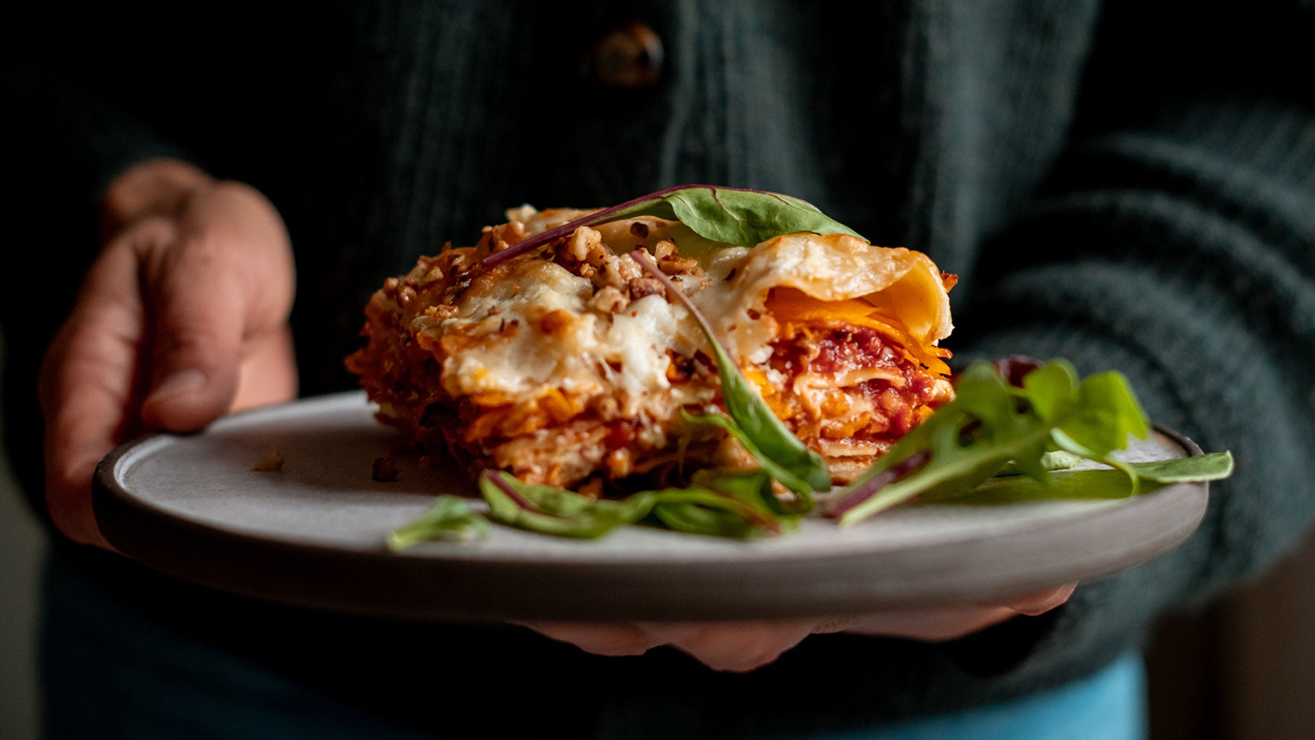 Ein Teller mit Lasagne und frischen grünen Salatblättern, in einer Hand gehalten.