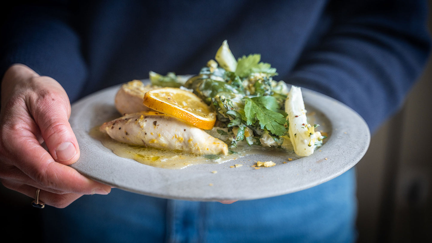 Gefülltes Hähnchen, Orangenscheibe und Salat mit Salzzitronen auf einem Teller in der Hand.