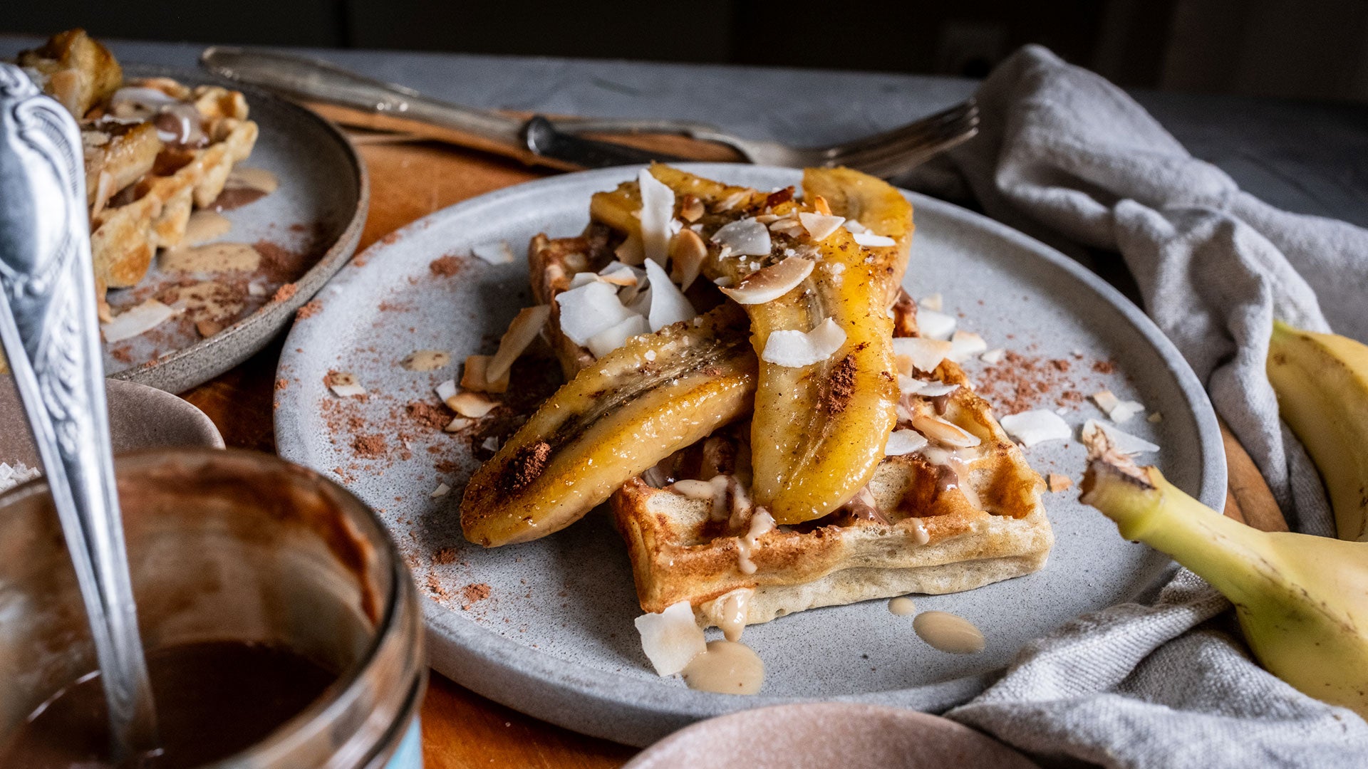 Waffeln mit karamellisierten Bananen, Kokosflocken und tropischer Sauce auf einem Teller.
