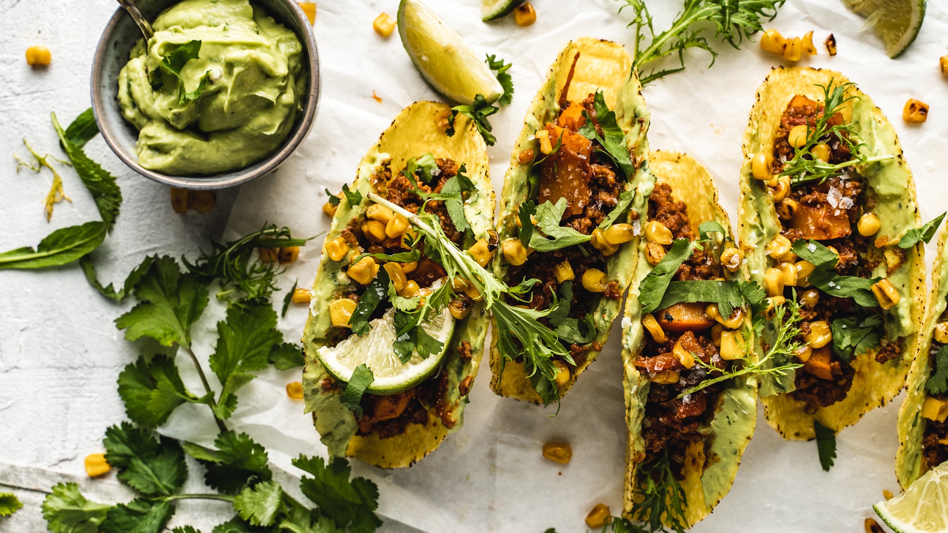 Drei Gemüsetacos mit Mais, Koriander und Limettenscheiben, dazu frische Guacamole.