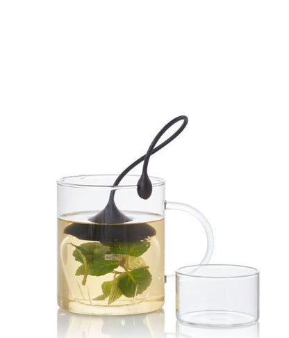 Teefilter Fusion von AdHoc in einem Glas mit Tee und Kräutern, daneben ein transparenter Deckel.