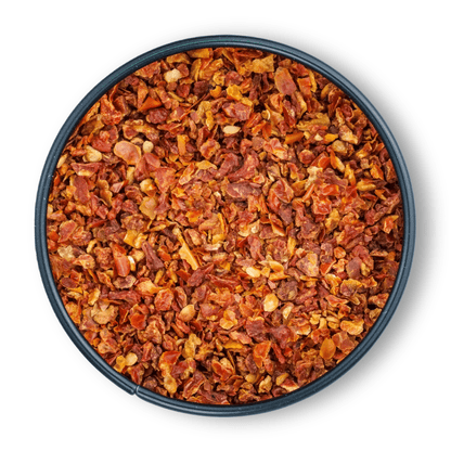 Schale mit groben Bio Tomatenflocken und Chili-Flocken auf weißem Hintergrund, Draufsicht.